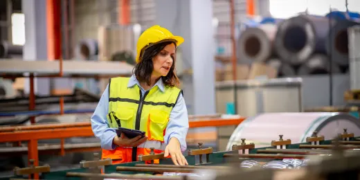 Manufacturing inspector in a hard hat and safety vest inspecting machinery in a manufacturing facility.