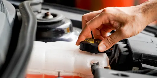 An engineer's hand opening a car coolant reservoir cap under the hood for maintenance.